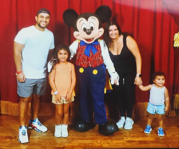 Daniel Patiño stands next to Mickey Mouse with his wife and two young daughters at Disney World