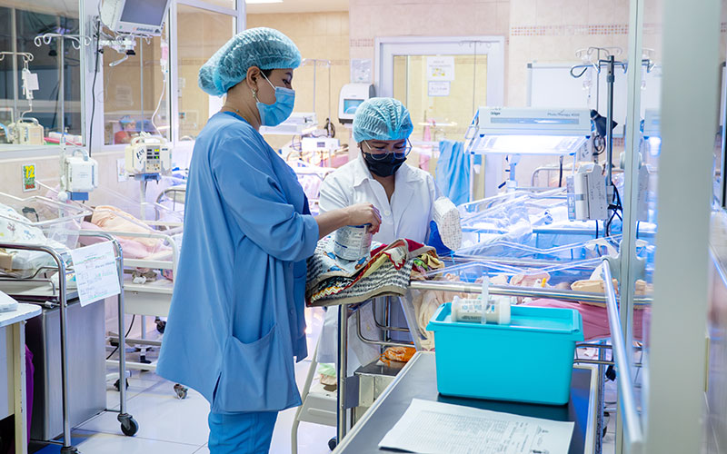 Two women dressed in a hospital gown, in a clinical setting.