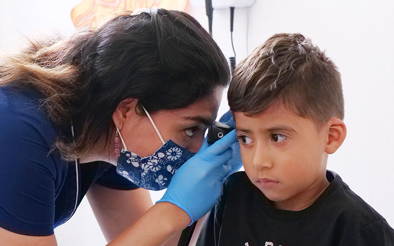 A woman is closely examining a young boy's ear.