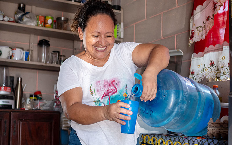 A woman pours water into a blue plastic container.